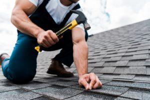 cropped view of handyman in uniform holding hammer while repairing roof